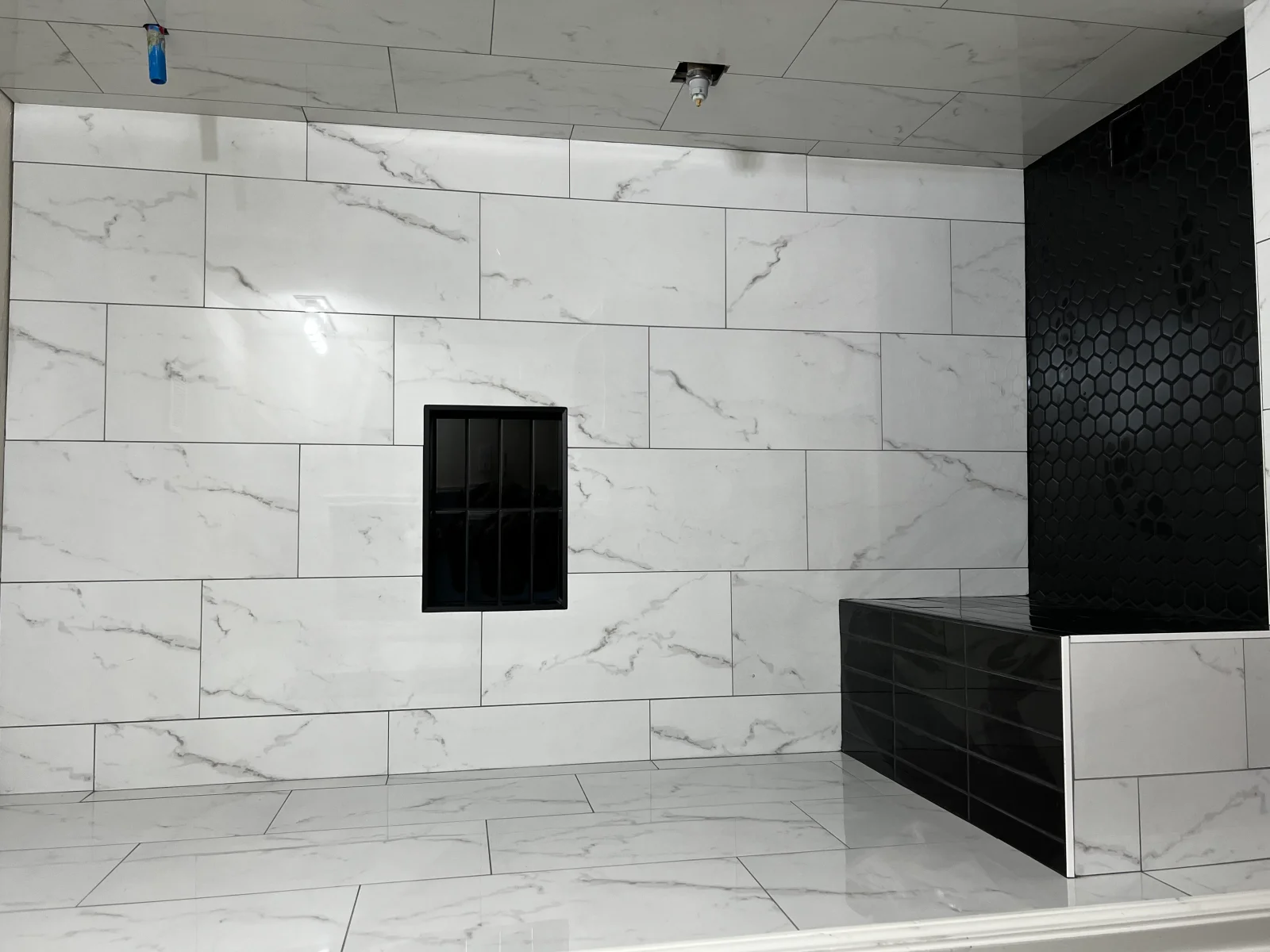 White marble subway tile shower walls with black hexagonal mosaic and subway tile accent