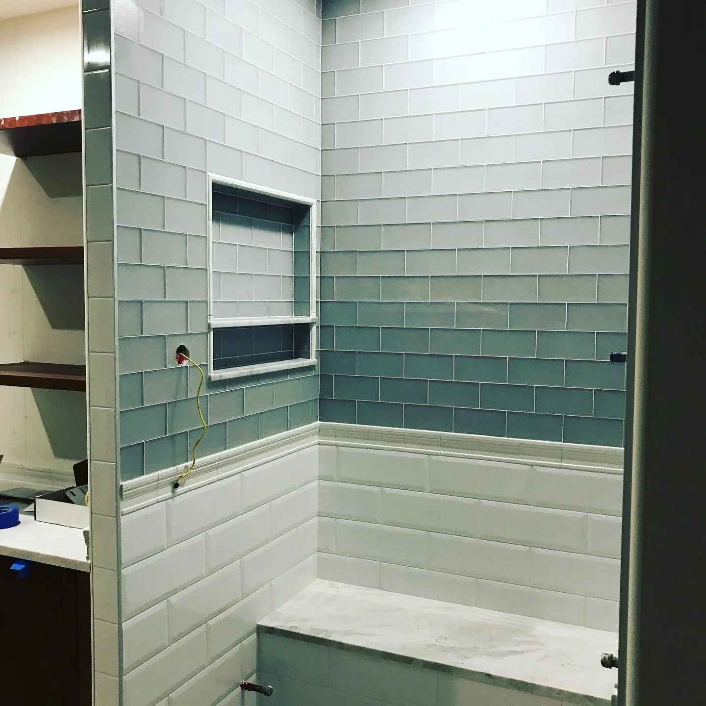 Shower enclosure with white and seafoam green subway tile, built-in niche, and black fixtures