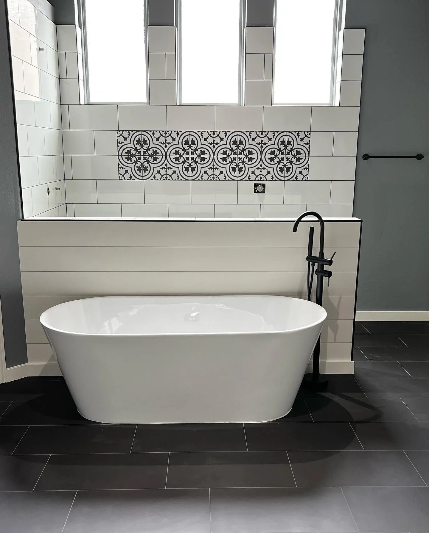 White subway tile walls with black geometric patterned accent band, dark slate floor, freestanding tub
