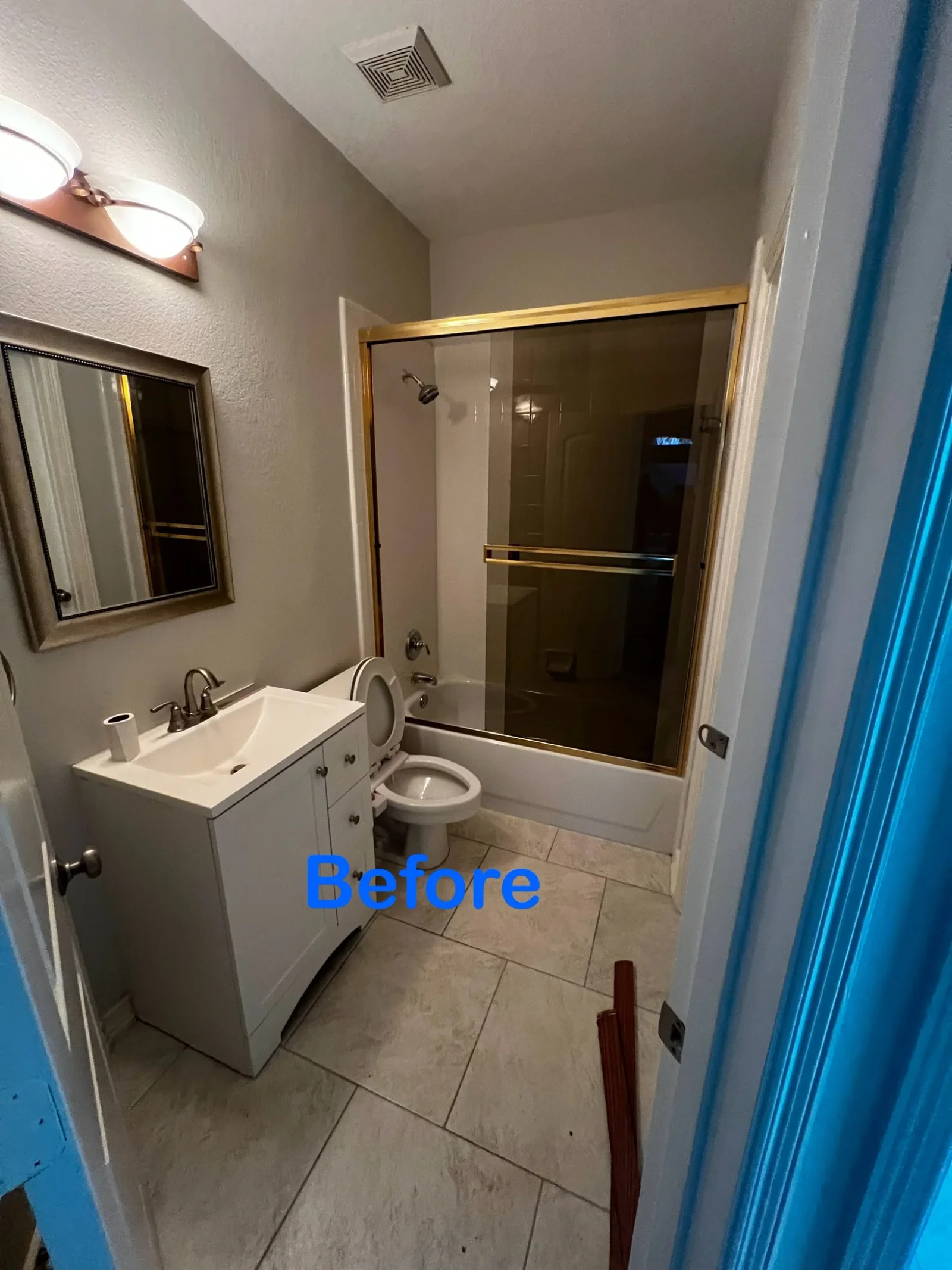Bathroom with ceramic tile flooring, glass shower enclosure with gold frame, white vanity sink, and toilet