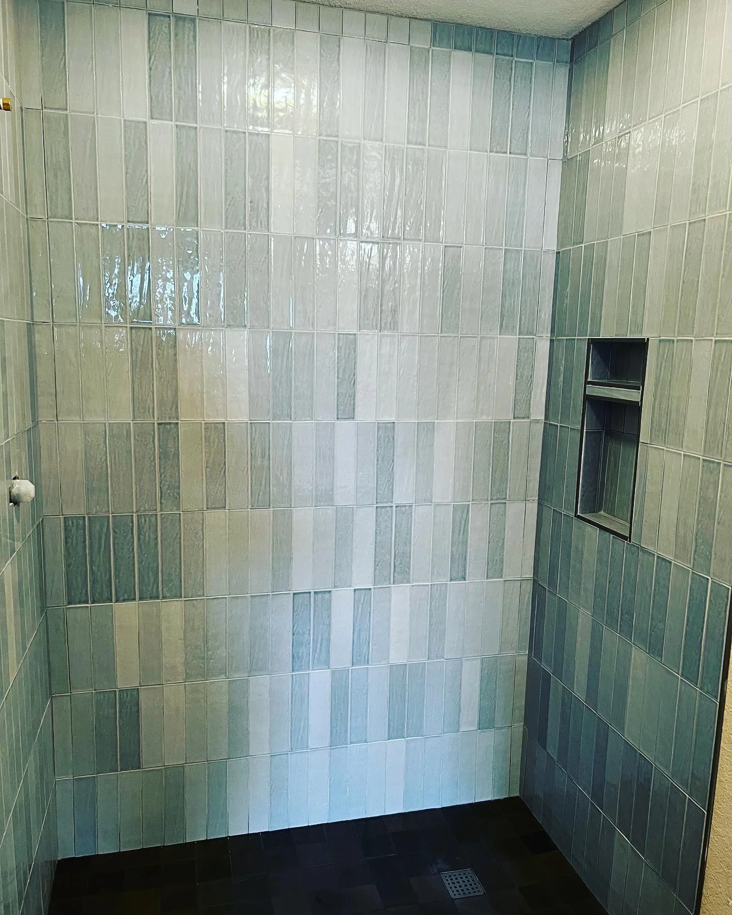 Vertical subway tile shower walls in green and cream tones with built-in niche