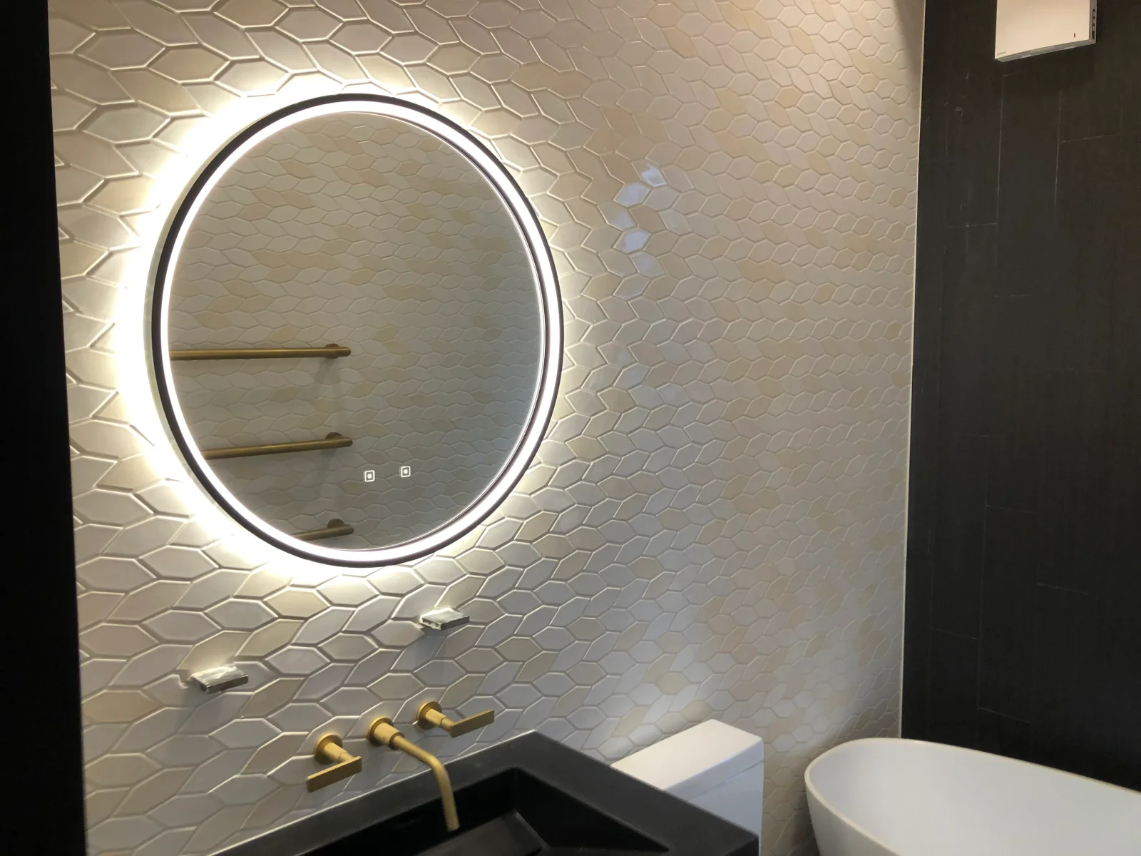 Cream hexagon ceramic tile wall with LED-lit round mirror and brass fixtures