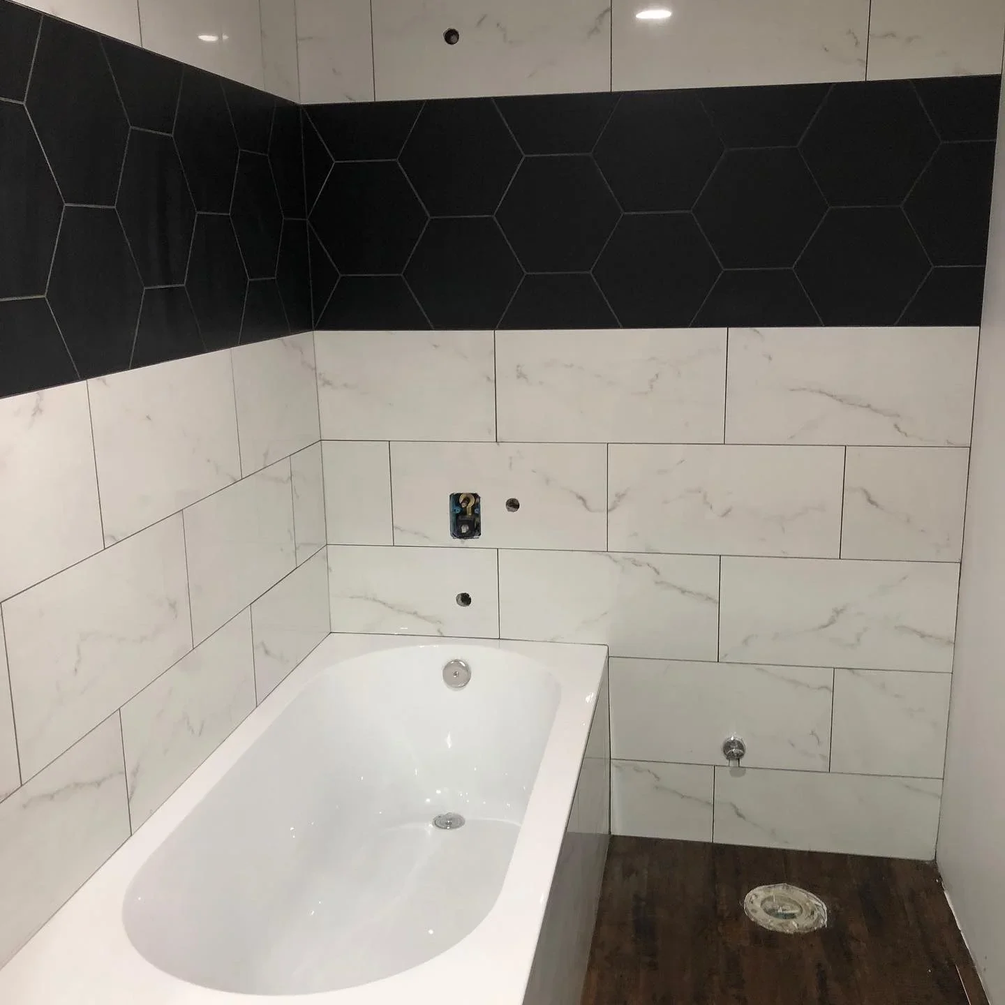 Bathroom with marble porcelain wall tiles, black hexagonal accent band, and white soaking tub