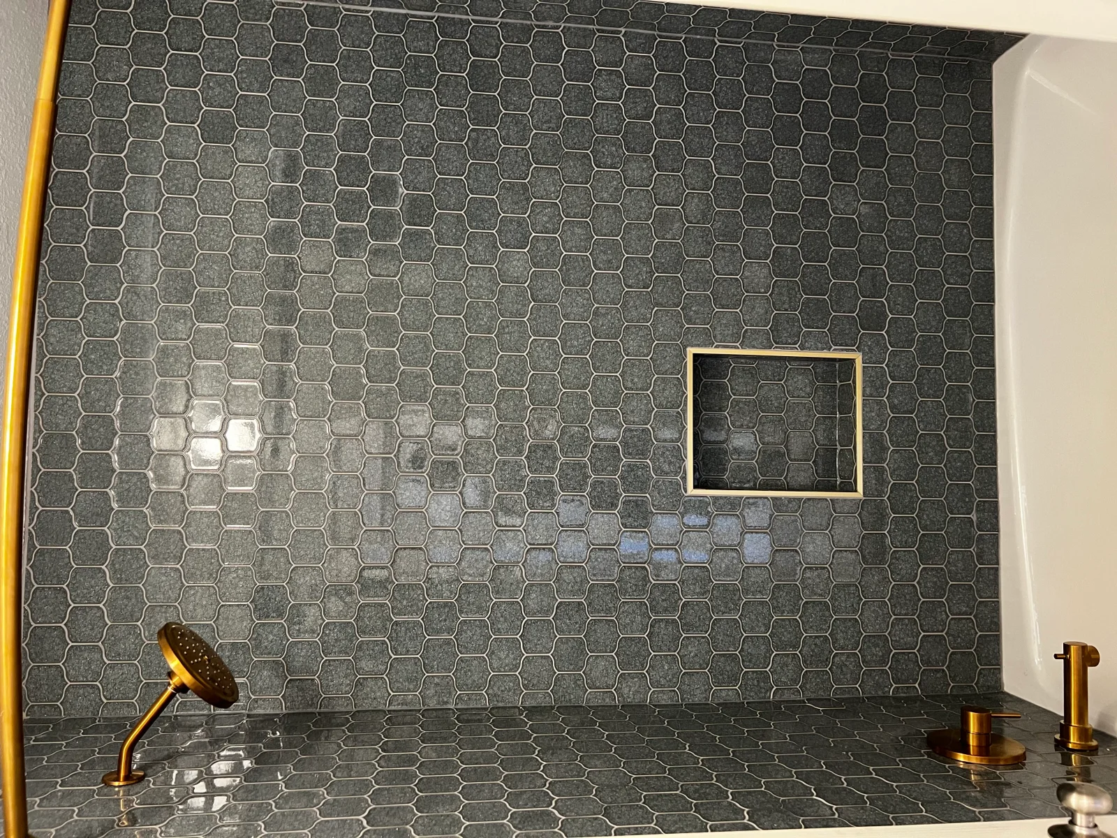 Charcoal hexagonal tile shower with brass fixtures and recessed niche