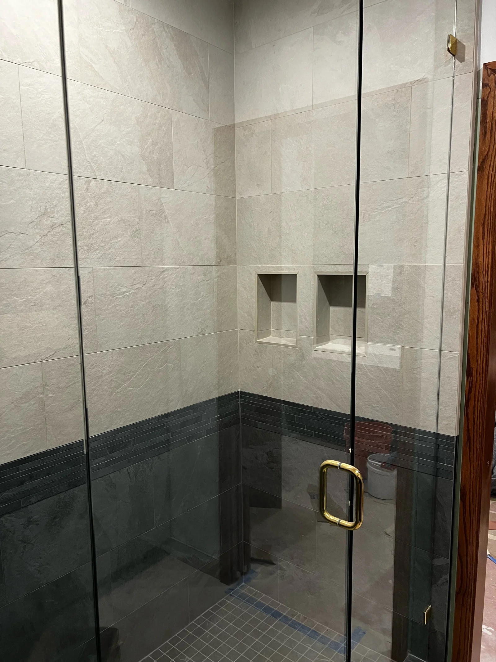 Walk-in shower with gray marble and dark slate tile, frameless glass doors, brass hardware, and built-in niches