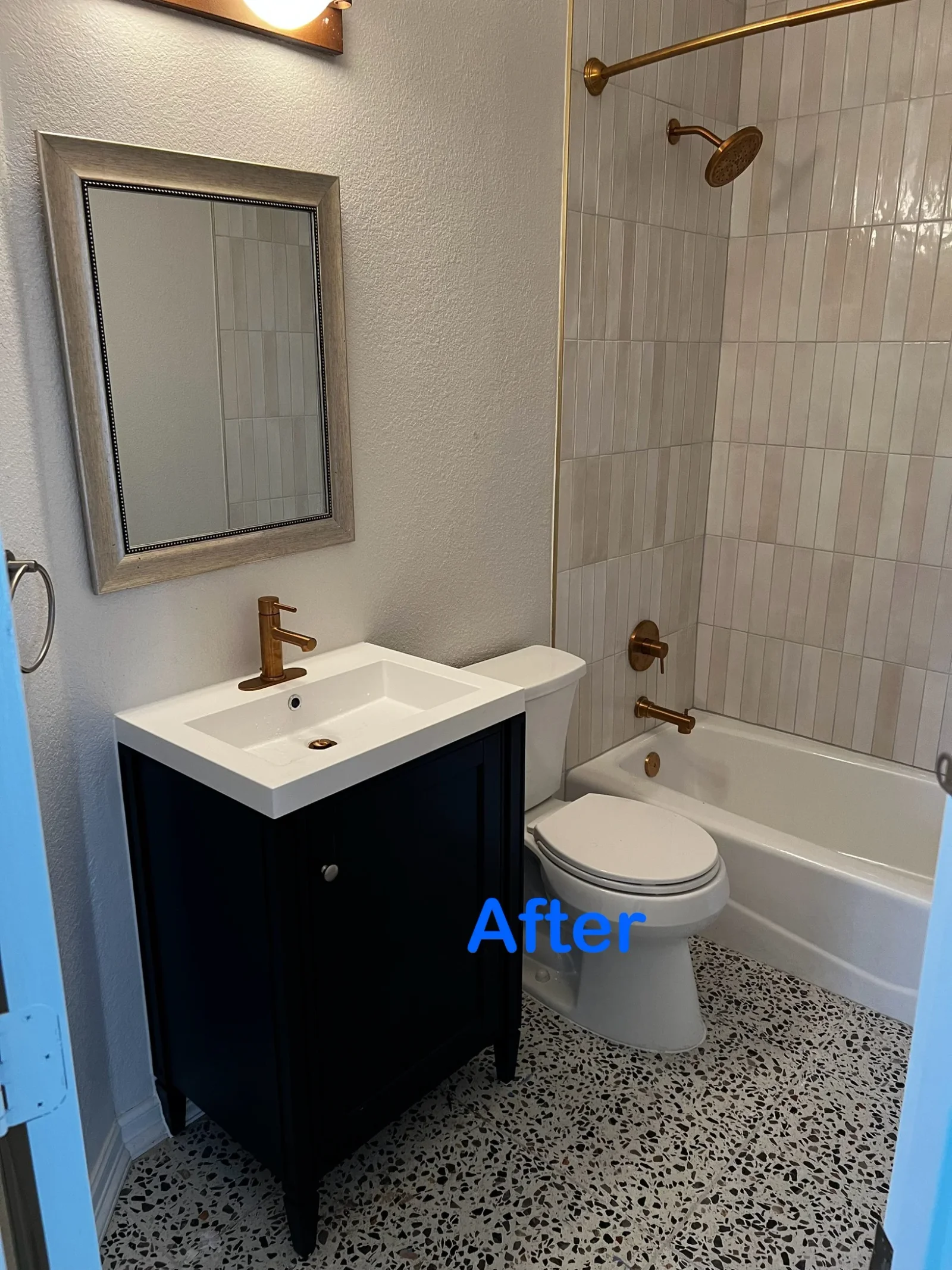 Bathroom with vertical gray tile shower surround, terrazzo floor, black vanity, and bronze fixtures